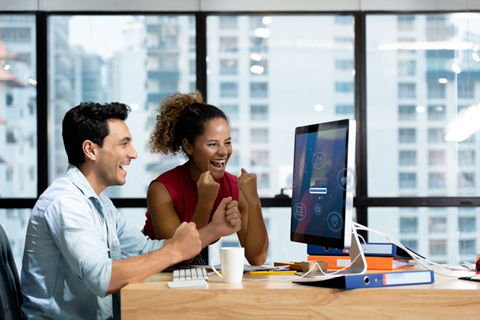 A Man and Woman Sit at a Desk and Cheer About What They See on the Computer Screen 