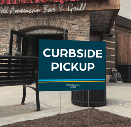 A brick restaurant with a yard sign out front that reads “Curbside Pickup.”