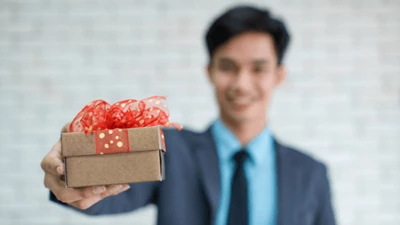 A Man Dressed in Business Professional Attire Offers a Box with a Gift Bow on it 