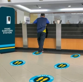 A Man Stands at a Reception Counter and There Are Floor Graphics Providing Social Distancing Cues on the Floor
