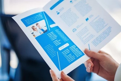 A photo of someone holding a half-fold brochure with a blue background and white text.