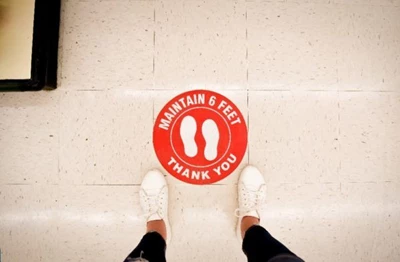 White shoes on a white floor with floor signage reading “maintain 6 feet thank you.”