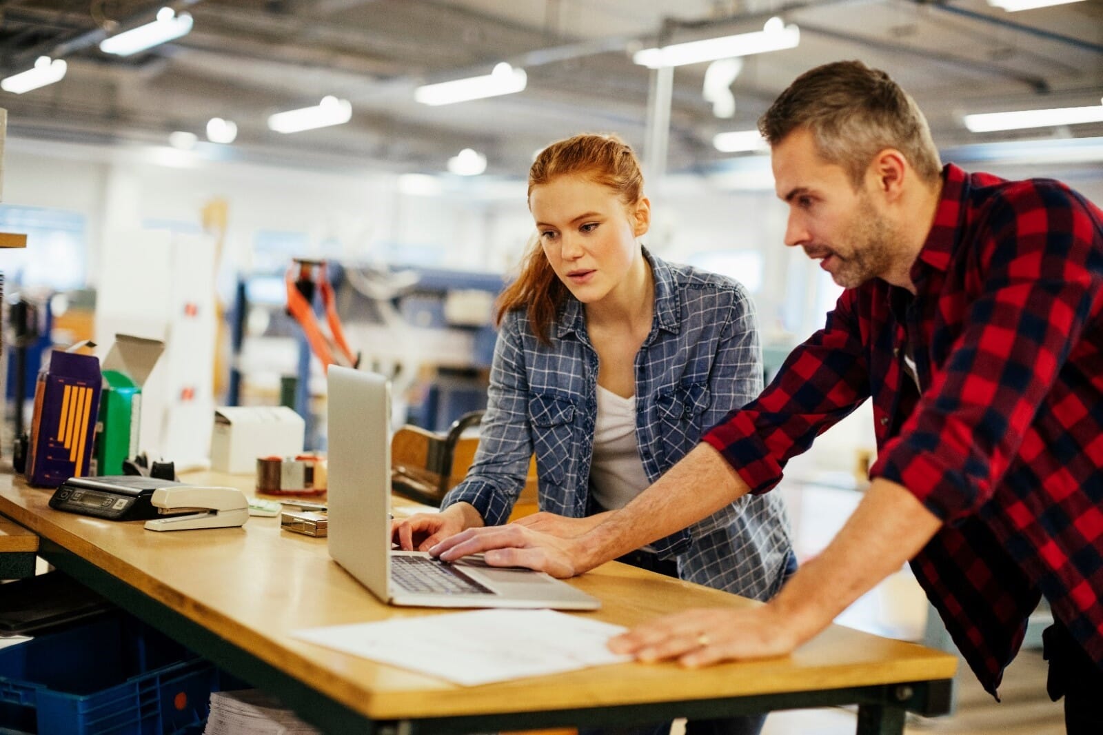 A man wearing red flannel and a woman wearing blue flannel looking at a laptop in a commercial printing