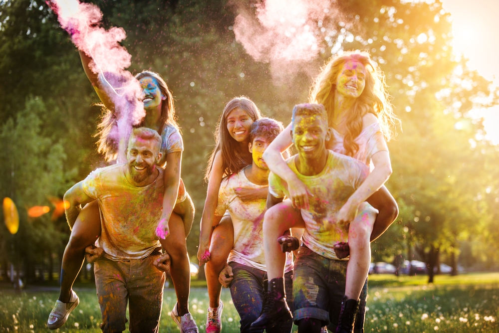 Group of happy friends playing with holi colors in a park - Young adults having fun at a holi festival, concepts about fun, fun and young generation